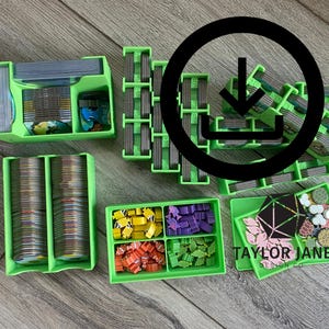 Op de afbeelding: Een verzameling groene plastic spelorganizers gevuld met spelstukken, kaarten en tokens. De organizers hebben verschillende vormen en maten, waaronder trays en kaarthouders. De tekst "TAYLOR JANE" is zichtbaar.
