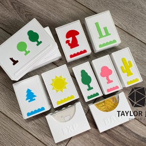 May include: White card holders with colorful nature-themed illustrations, including trees, a mushroom, and a sun. The cards are arranged on a wooden surface. The text "TAYLOR JANE DESIGN CO" is visible.
