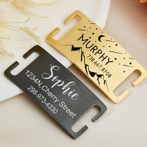May include: Two personalized pet ID tags. One is gold with a mountain and stars design and the text "MURPHY 738.667.8708". The other is black with the text "Sophie 1234N, Cherry Street 298-973-4330".
