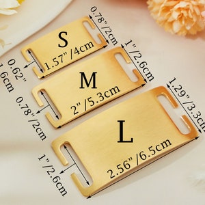 May include: Three gold-colored metal dog collar tags with different sizes labeled "S", "M", and "L". The tags have measurements in inches and centimeters.