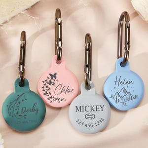 May include: Four personalized dog tags with different designs and names. The tags are round and made of a light blue, pink, and green material. The names on the tags are "Derby", "Chloe", "Mickey", and "Helen".