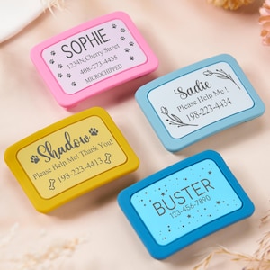 May include: Four colourful pet ID tags with rounded corners. The tags are pink, yellow, light blue, and dark blue. Each tag has a name, contact information, and the text "Please Help Me!" or "Thank You!" The tags are decorated with paw prints and floral designs.