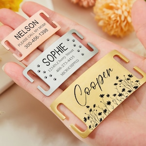 May include: Three personalized dog tags with different designs. The first tag is rose gold and says "NELSON PLEASE CALL MY MOM! 300-456-1398". The second tag is silver and says "SOPHIE 1234N, Cherry Street 408-273-4435 MICROCHIPPED" with paw prints. The third tag is gold and says "Cooper" with a floral design.