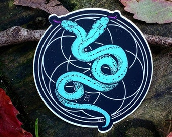 Op de afbeelding: Een sticker met een turquoiseblauwe slang met een geometrisch patroon, die zichzelf omslingert, op een zwarte achtergrond met een witte cirkel en een geometrisch ontwerp.