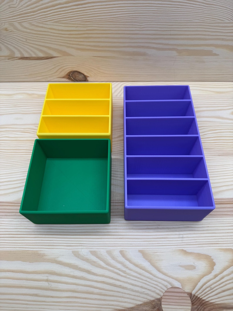May include: Four colorful plastic organizers in yellow, green, and purple. The yellow organizer has three compartments, the purple has five, and the green is a square tray. These are ideal for desk organization.