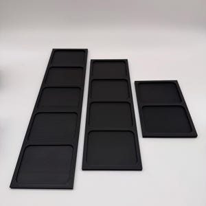 May include: Three black rectangular trays with multiple compartments. The trays are arranged in a row, varying in size and number of compartments. The trays are made of a matte black material and are set against a white background.