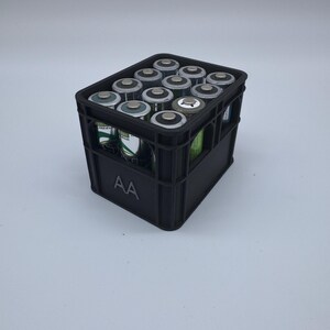 May include: A black plastic crate filled with AA batteries. The batteries are silver and black, and the crate has the letters "AA" printed on the side. The crate is sitting on a white surface.