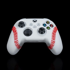 May include: White Xbox controller with a baseball-stitched design. The controller has red stitching and a white background.
