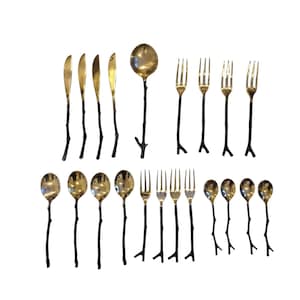 May include: A collection of gold-colored flatware with black branch-like handles. The set includes spoons, forks, and knives. The arrangement is displayed on a white surface, showcasing the elegant design of the utensils.