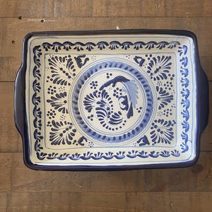 May include: Rectangular ceramic serving tray with a blue and white floral design. The tray has a dark blue border and handles. The center features a circular design with a bird motif. The tray is suitable for serving food.
