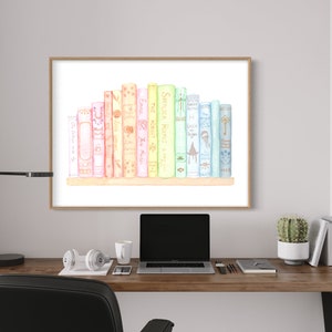 May include: Watercolour print of a collection of colourful books on a shelf. The books are in shades of pink, yellow, green, and blue. The artwork is framed in a light brown frame and hangs on a grey wall above a wooden desk.