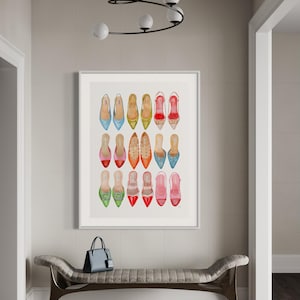 Op de afbeelding: Een ingelijst afdruk van een aquarel van 18 kleurrijke damesschoenen. De schoenen zijn allemaal in verschillende stijlen en kleuren en zijn gerangschikt in een rasterpatroon. De afdruk hangt aan een muur in een gang.