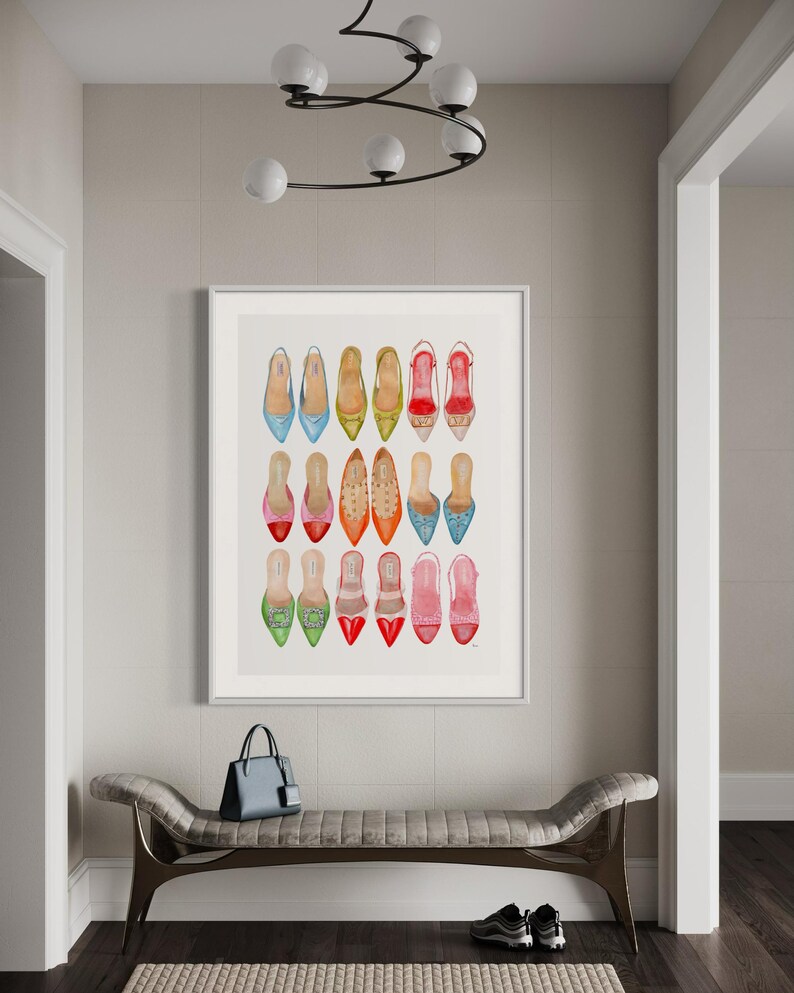 Op de afbeelding: Een ingelijst afdruk van een aquarel van 18 kleurrijke damesschoenen. De schoenen zijn allemaal in verschillende stijlen en kleuren en zijn gerangschikt in een rasterpatroon. De afdruk hangt aan een muur in een gang.