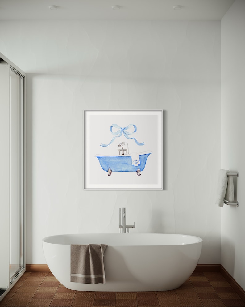 Peut inclure: Une peinture &agrave; l'aquarelle d'une baignoire bleue avec une serviette blanche et un n&oelig;ud bleu sur le dessus. La baignoire a quatre pieds et un robinet. La peinture est encadr&eacute;e en blanc.