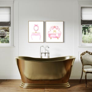 May include: Two framed watercolor illustrations of a pink vanity set and a pink bathtub with a large pink bow on each. The illustrations are hung on a white wall in a bathroom setting.
