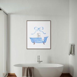 May include: A framed wall art print featuring a watercolor illustration of a blue claw-foot bathtub with a silver faucet and a white towel draped over the side. A large, light blue ribbon bow is positioned directly above the bathtub illustration.