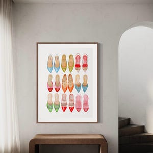 Op de afbeelding: Een ingelijst afdruk van een aquarelillustratie van 18 kleurrijke damesschoenen. De schoenen zijn gerangschikt in drie rijen van zes, waarbij elke rij een ander kleurenschema heeft. De schoenen zijn allemaal spitse ballerina's.