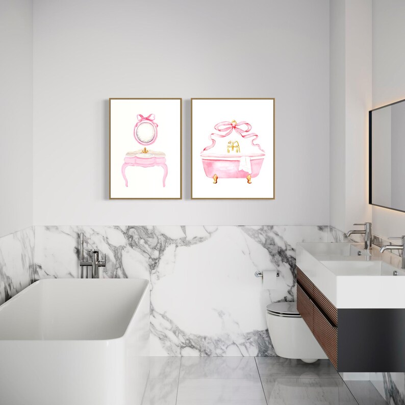 May include: Two watercolor paintings in gold frames, one depicting a pink vanity with a mirror and the other a pink bathtub with a bow. The paintings are hung on a white wall above a white marble countertop.