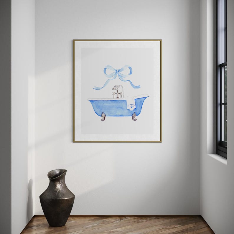 May include: A framed watercolor print featuring a blue clawfoot bathtub with a silver faucet and a white towel draped over the side. A large, light blue ribbon bow is positioned directly above the bathtub against a plain white background.