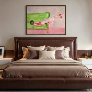 May include: Watercolor painting of a person reclining on a green sofa, wearing a red top and pink striped skirt, with red heels. The artwork is framed and hangs above a brown leather bed with pillows.