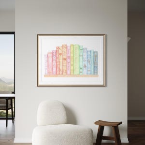 May include: A framed watercolour print featuring a collection of colourful books on a wooden shelf. The books are in shades of pink, orange, yellow, green, and blue. The print is displayed on a light grey wall, with a white chair and wooden stool in the foreground.