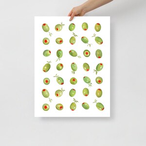 May include: A watercolor print featuring a pattern of green olives with red centers and small sprigs. The olives are arranged on a white background. The print is held by a person's hand.