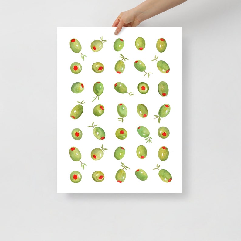 May include: A watercolor print featuring a pattern of green olives with red centers and small sprigs. The olives are arranged on a white background. The print is held by a person's hand.