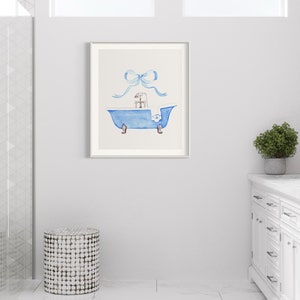 Peut inclure: Une peinture &agrave; l'aquarelle d'une baignoire bleue avec un cadeau blanc &agrave; l'int&eacute;rieur et un ruban bleu sur le dessus. La peinture est encadr&eacute;e dans un cadre blanc et est accroch&eacute;e &agrave; un mur blanc.