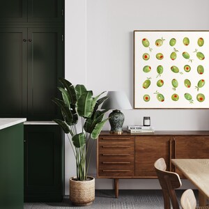 May include: A framed watercolor print featuring green olives with red centers and small sprigs. The artwork hangs above a wooden sideboard in a dining room setting. A large potted plant and a table are also visible.