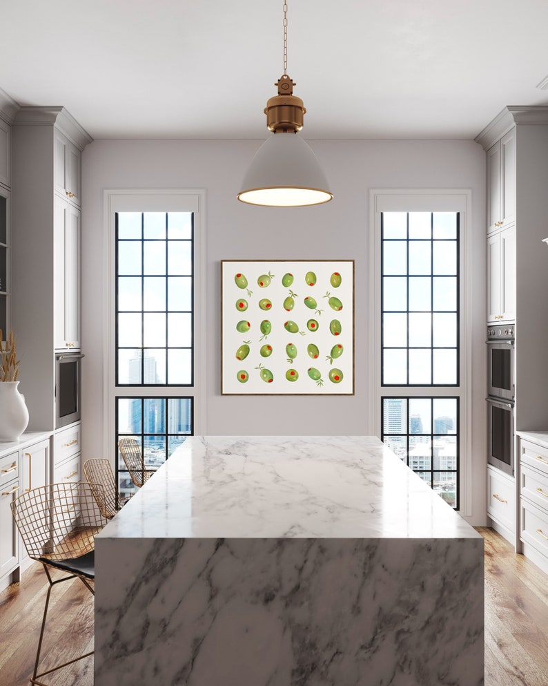 May include: A modern kitchen with a marble island and a framed print of green olives. The print hangs above the island, and a white pendant light hangs from the ceiling. Two windows offer a view of a cityscape.