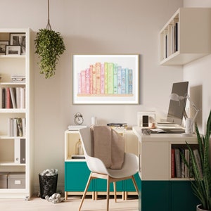 May include: A framed print featuring a collection of colourful books. The books are arranged on a wooden shelf, with a gold frame. The spines of the books are in shades of pink, yellow, green, and blue. The print is displayed in a modern office setting.