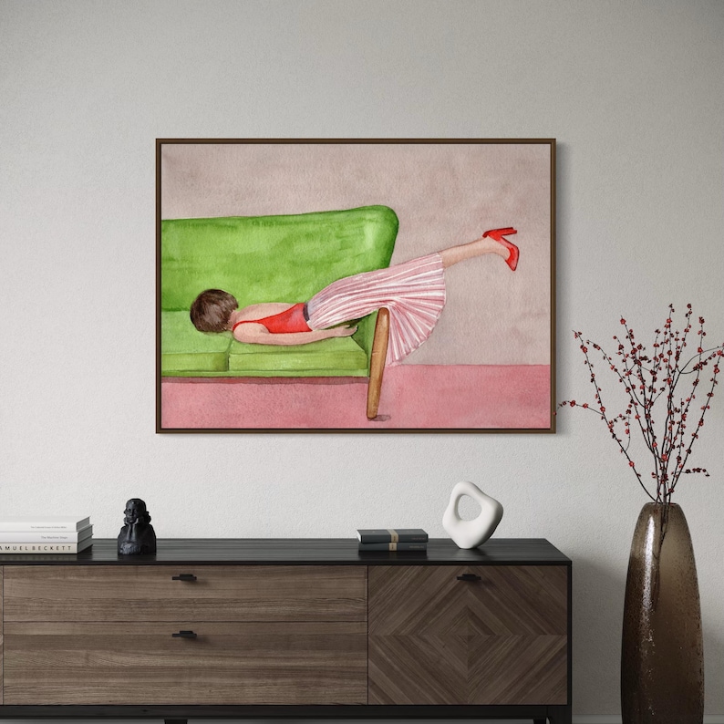 May include: Watercolor painting of a person reclining on a green sofa. The person wears a red top, a pink and white striped skirt, and red heels. The artwork is framed in a dark brown frame and hangs on a neutral wall.