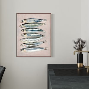 May include: A framed art print featuring a watercolor illustration of seven sardines arranged vertically. The fish have silver bodies with blue and green highlights, set against a pale pink background. The frame is a dark brown color.
