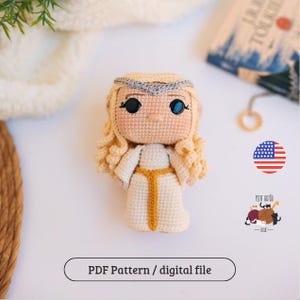 Pode incluir: Boneca de crochê feita à mão com cabelo loiro encaracolado, vestindo um vestido branco com cinto dourado e uma faixa de cabeça prateada. A boneca tem olhos pretos grandes com reflexos azuis. O texto "PDF Pattern / digital file" está na parte inferior.