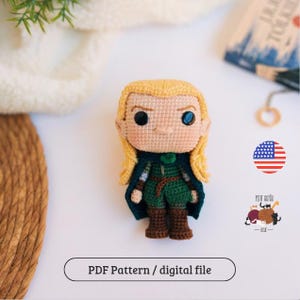 Pode incluir: Boneca de crochê feita à mão com cabelo loiro, vestindo uma túnica verde, uma capa azul escura e botas marrons. A boneca tem olhos grandes e pretos e um pequeno sorriso. O texto "PDF Pattern / digital file" está abaixo.