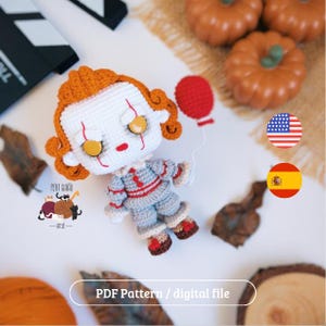 Pode incluir: Boneca de palhaço de crochê com cabelo laranja, rosto branco e detalhes vermelhos. A boneca usa uma roupa cinza e vermelha e segura um balão vermelho. Tema de Halloween.