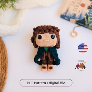 Pode incluir: Boneca de crochê de um personagem com cabelo castanho, uma capa verde e roupas marrons. A boneca tem olhos grandes e pretos com reflexos azuis. A boneca está em uma superfície branca. O texto "PDF Pattern / digital file" está abaixo.
