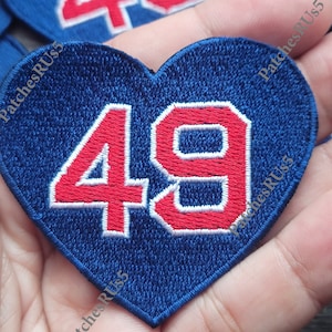 May include: A blue heart-shaped patch with the number 49 in red with white outlines. The patch is embroidered and has the text "PatchesRUS5" on the bottom.