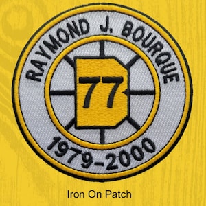 May include: White and yellow iron-on patch with a hockey puck design. The patch features the text "Raymond J. Bourque" and the number "77" in a black font. The text "1979-2000" is also included on the patch.