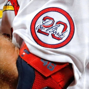 May include: A white baseball jersey with a red circle containing the number "20" and the name "Albert Pujols" in black lettering.