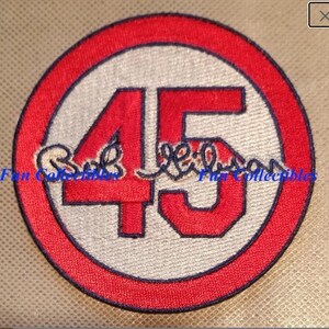 May include: Red and white embroidered baseball patch with the number 45 in the center. The number is outlined in black and the patch has a blue border. The signature "Bob Gibson" is embroidered in black below the number.