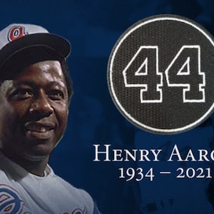 May include: A black and white photo of baseball player Henry Aaron wearing a white baseball uniform with a blue and red Atlanta Braves logo. He is wearing a baseball cap with the Atlanta Braves logo. A black circle with a white number 44 is in the upper right corner of the image. The text "HENRY AARON 1934 - 2021" is below the circle.