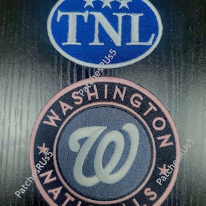 May include: Two embroidered patches. The top patch is blue with white text reading "TNL" and three stars. The bottom patch is a circular design with "WASHINGTON NATIONALS" around a "W" logo. The text "IRON ON" is at the bottom.