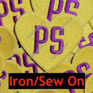 May include: A close-up of multiple yellow heart-shaped iron-on patches with the letters "PS" in purple. The text "Iron/Sew On" is printed in red at the bottom of the image.
