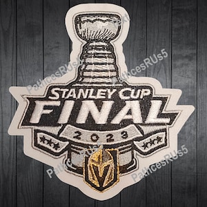 May include: A white patch with a silver Stanley Cup Final logo. The logo features the Stanley Cup trophy, the words "Stanley Cup Final", and the year "2023". The patch also features a Vegas Golden Knights logo.