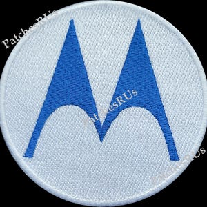 May include: White embroidered patch with a blue stylized 'M' logo.