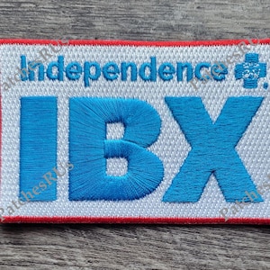 May include: White embroidered patch with red trim. The patch features the text "Independence" and a small red cross. The text "IBX" is embroidered in blue.