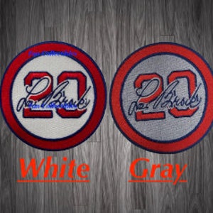 May include: Four embroidered patches with the number 20 and the name "Lou Brock" in red and blue lettering. The patches are on different colored backgrounds: cream, white, gray, and blue.