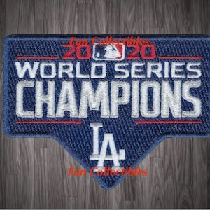 May include: A blue and red embroidered patch with the text "2020 World Series Champions LA" in white lettering. The patch is shaped like a triangle with a rounded top.