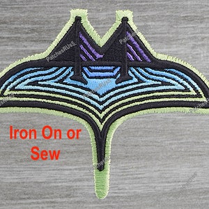 May include: An embroidered iron-on or sew-on patch featuring a stylized manta ray in shades of blue, purple, and green. The patch has a black outline and a light green border. The text "Iron On or Sew" is printed below the patch.